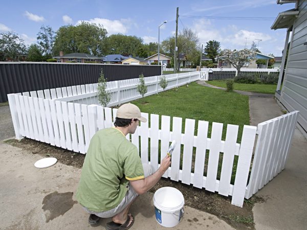 Man painting a white picket fence on a sunny day
