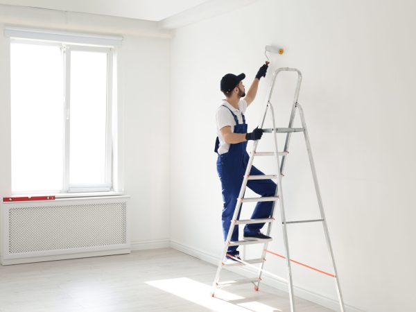 Handyman painting wall with roller brush indoors, space for text. Professional construction tools