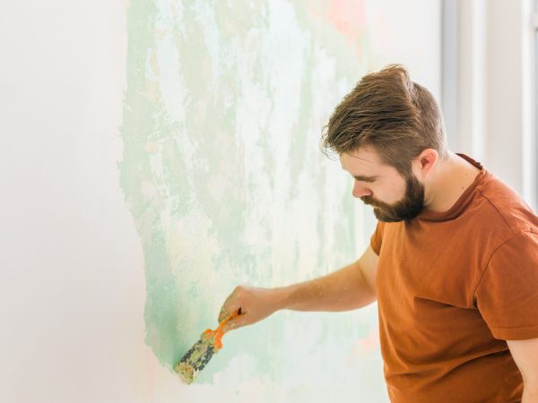 Man smoothes wall surface with a wall grinder. Male grind a white plaster wall - renovation and redecoration